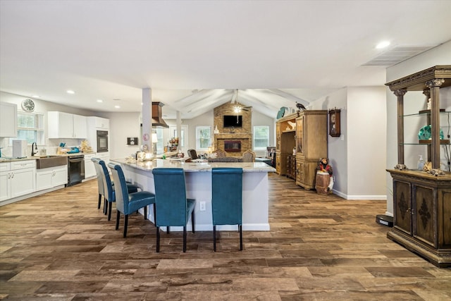 kitchen featuring black appliances, exhaust hood, white cabinetry, a kitchen breakfast bar, and hardwood / wood-style flooring