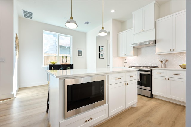 kitchen featuring gas range, black microwave, pendant lighting, decorative backsplash, and white cabinets