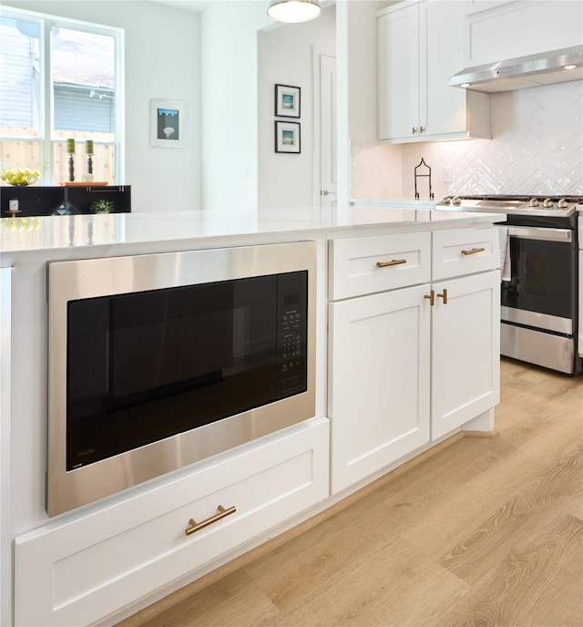 kitchen featuring stainless steel range with gas cooktop, built in microwave, white cabinetry, tasteful backsplash, and light hardwood / wood-style flooring