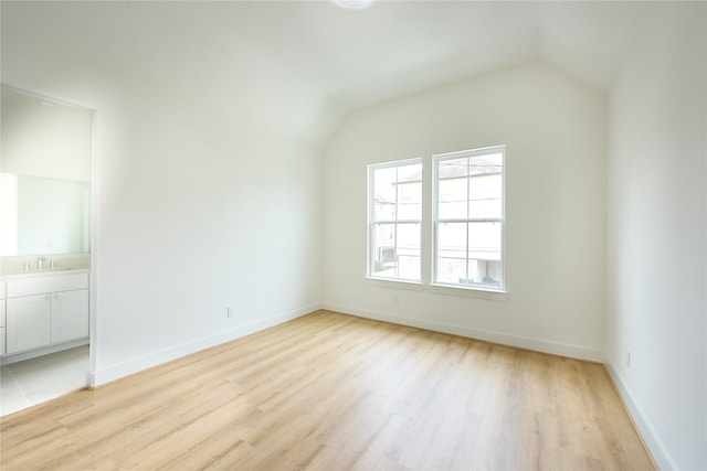 empty room featuring sink, vaulted ceiling, and light wood-type flooring