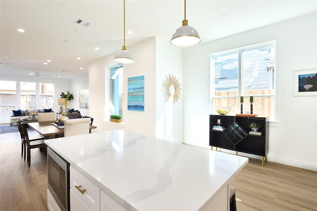 kitchen featuring hanging light fixtures, stainless steel microwave, white cabinets, and light hardwood / wood-style flooring