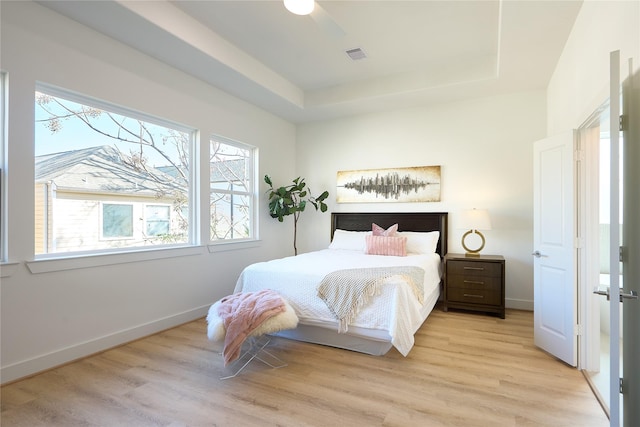 bedroom with light hardwood / wood-style flooring, a raised ceiling, and ceiling fan