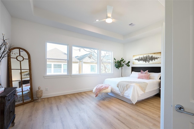 bedroom with a raised ceiling and light wood-type flooring