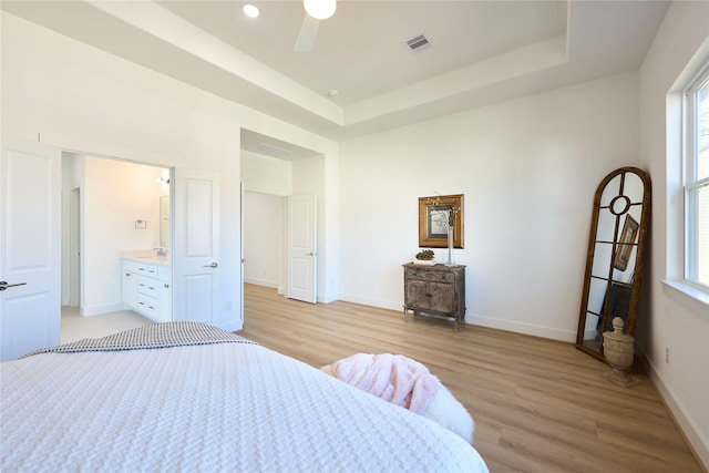 bedroom with ceiling fan, a tray ceiling, and light hardwood / wood-style floors