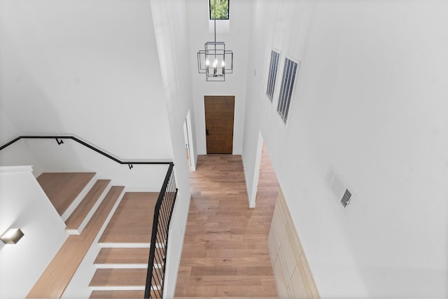 stairs with hardwood / wood-style flooring, a chandelier, and a high ceiling