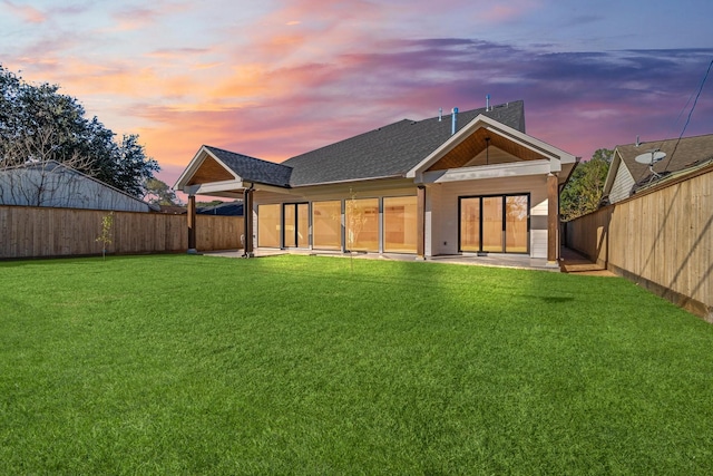 back house at dusk with a patio area and a lawn