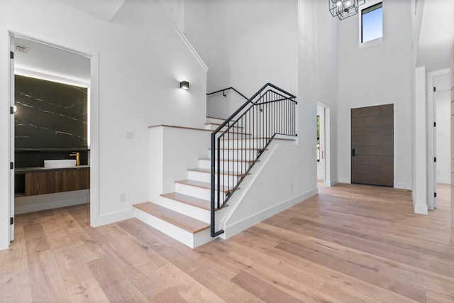 foyer with an inviting chandelier, a towering ceiling, and light wood-type flooring