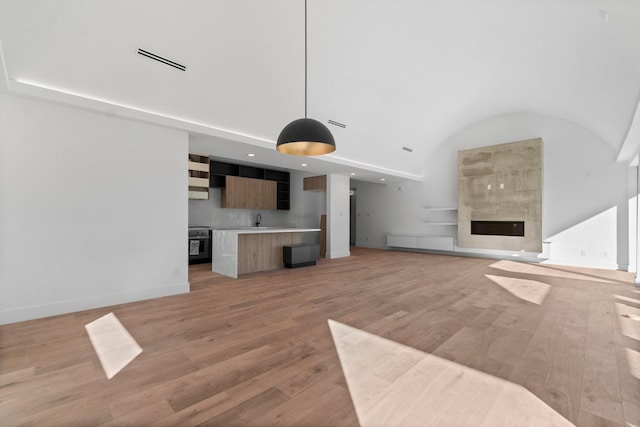 unfurnished living room with a towering ceiling, a tiled fireplace, sink, and light wood-type flooring