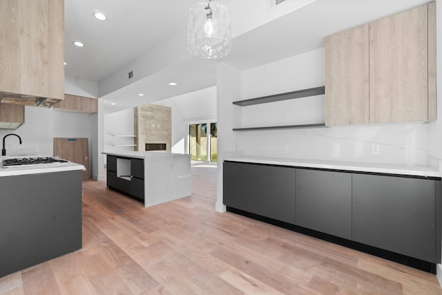 kitchen with pendant lighting, backsplash, light hardwood / wood-style floors, a large fireplace, and light brown cabinets