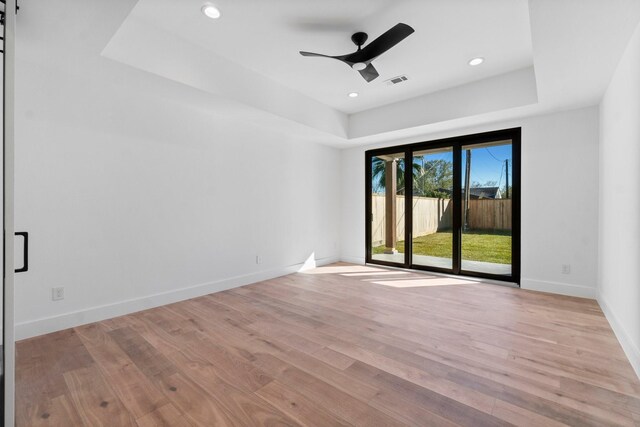 empty room with a tray ceiling, light hardwood / wood-style flooring, and a barn door