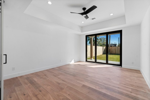 unfurnished room with a barn door, a raised ceiling, and light wood-type flooring