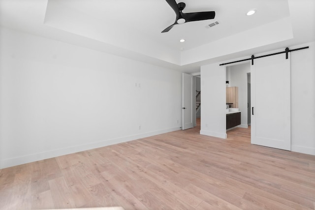 unfurnished bedroom with a barn door, a tray ceiling, and light hardwood / wood-style floors