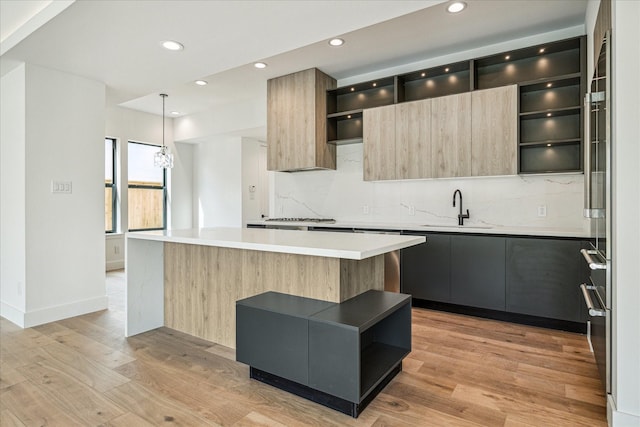 kitchen featuring a kitchen island, decorative light fixtures, sink, decorative backsplash, and light hardwood / wood-style floors