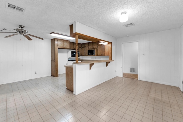 kitchen with a kitchen bar, a textured ceiling, kitchen peninsula, and ceiling fan