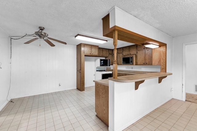 kitchen featuring electric range, kitchen peninsula, built in microwave, and a textured ceiling