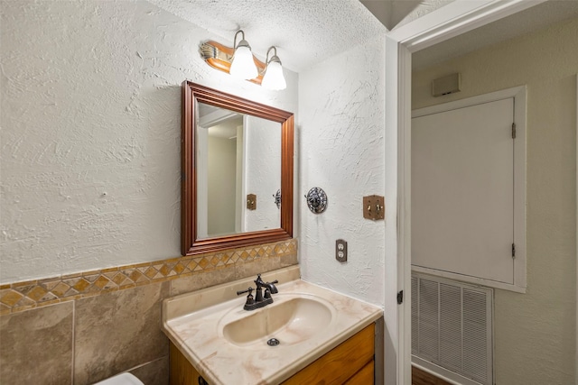 bathroom with a textured ceiling, vanity, and tile walls