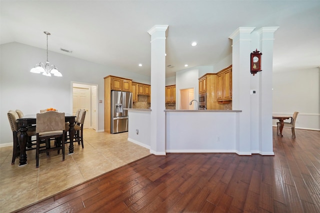 kitchen with hardwood / wood-style floors, appliances with stainless steel finishes, decorative columns, an inviting chandelier, and kitchen peninsula