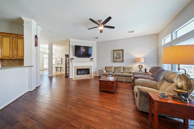 living room with decorative columns, dark wood-type flooring, ceiling fan, and a fireplace