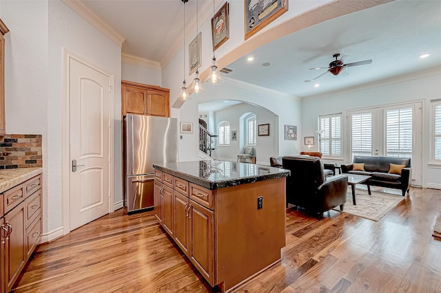 kitchen with dark stone countertops, pendant lighting, stainless steel fridge, and light hardwood / wood-style flooring