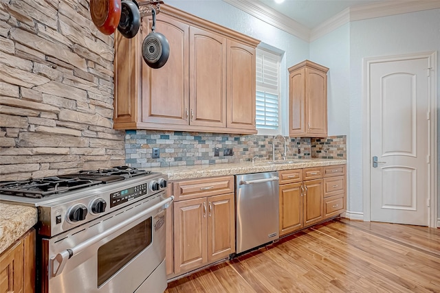 kitchen with sink, appliances with stainless steel finishes, ornamental molding, light stone countertops, and light wood-type flooring