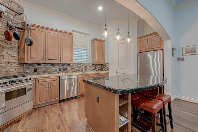 kitchen featuring crown molding, decorative light fixtures, dark stone countertops, appliances with stainless steel finishes, and a kitchen island