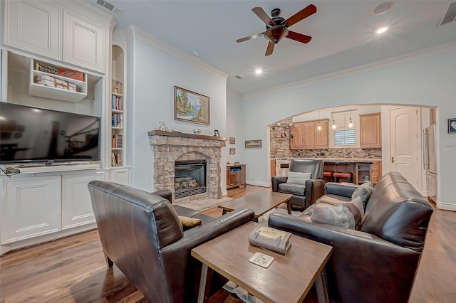 living room with crown molding, ceiling fan, a stone fireplace, and light hardwood / wood-style floors