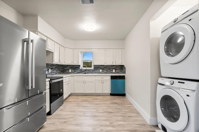 kitchen with stacked washer / dryer, white cabinetry, stainless steel appliances, light hardwood / wood-style floors, and backsplash