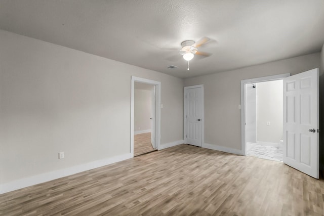 unfurnished bedroom featuring a closet, light wood-type flooring, connected bathroom, and ceiling fan