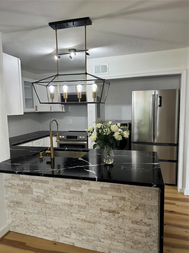 kitchen with stainless steel appliances, white cabinetry, a textured ceiling, and wood-type flooring