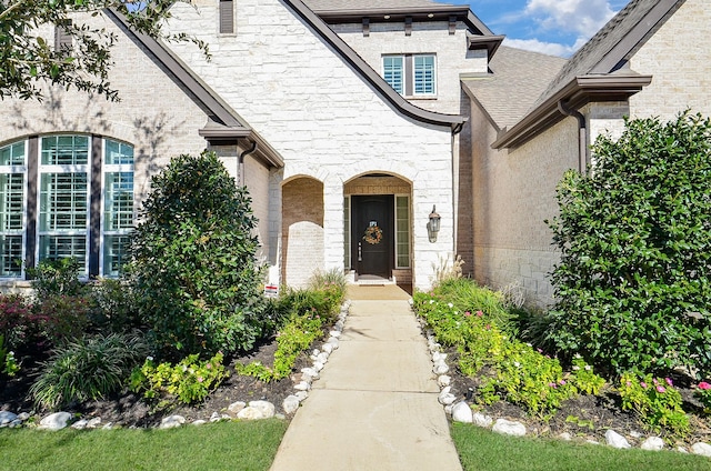 doorway to property with brick siding and a shingled roof