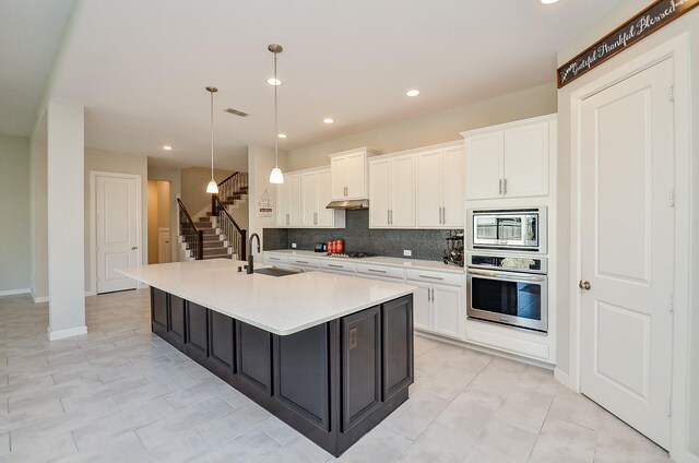 kitchen with appliances with stainless steel finishes, hanging light fixtures, a kitchen island with sink, sink, and white cabinets