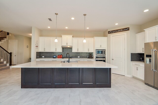 kitchen featuring white cabinets, decorative light fixtures, stainless steel appliances, sink, and a center island with sink