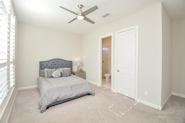 bedroom with ceiling fan, light colored carpet, and ensuite bath