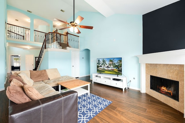 living room with a tiled fireplace, dark hardwood / wood-style floors, high vaulted ceiling, and ceiling fan