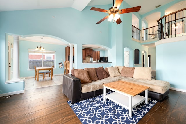 living room featuring decorative columns, ceiling fan with notable chandelier, high vaulted ceiling, and wood-type flooring