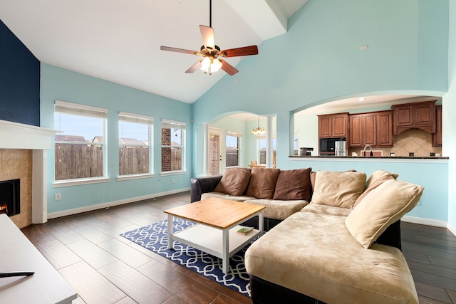 living room featuring high vaulted ceiling, wood-type flooring, a tile fireplace, and ceiling fan