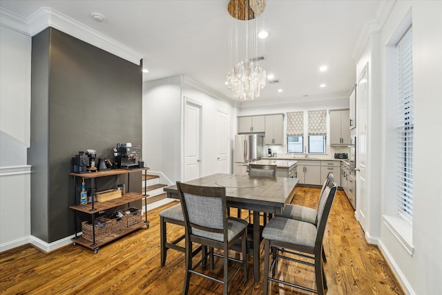 dining space with light hardwood / wood-style flooring, crown molding, and a notable chandelier