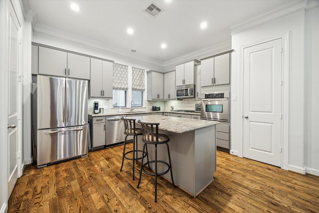 kitchen featuring dark hardwood / wood-style flooring, appliances with stainless steel finishes, tasteful backsplash, a kitchen island, and a breakfast bar area