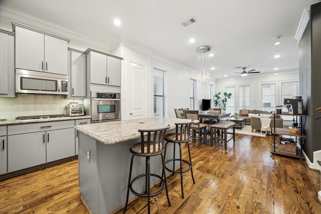 kitchen featuring a center island, appliances with stainless steel finishes, tasteful backsplash, wood-type flooring, and a breakfast bar