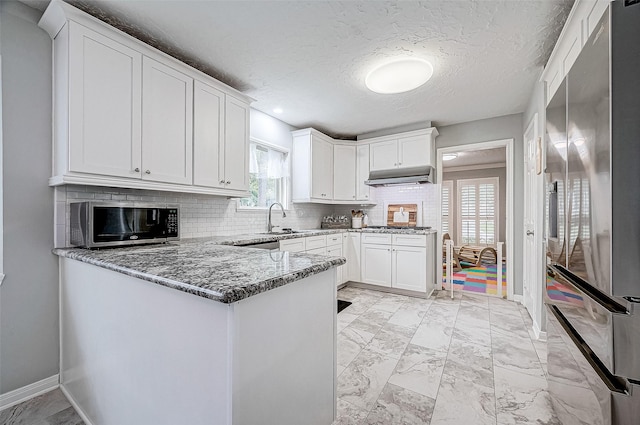 kitchen with appliances with stainless steel finishes, dark stone counters, white cabinets, kitchen peninsula, and backsplash