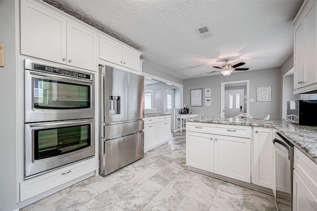 kitchen with ceiling fan, light stone countertops, a textured ceiling, white cabinetry, and stainless steel appliances