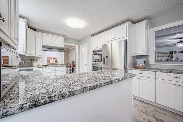 kitchen featuring a textured ceiling, white cabinets, stainless steel appliances, dark stone counters, and ceiling fan