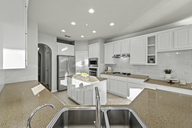 kitchen with decorative backsplash, light stone counters, white cabinets, and stainless steel appliances