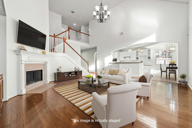 living room with a tiled fireplace, light hardwood / wood-style floors, a high ceiling, and a notable chandelier