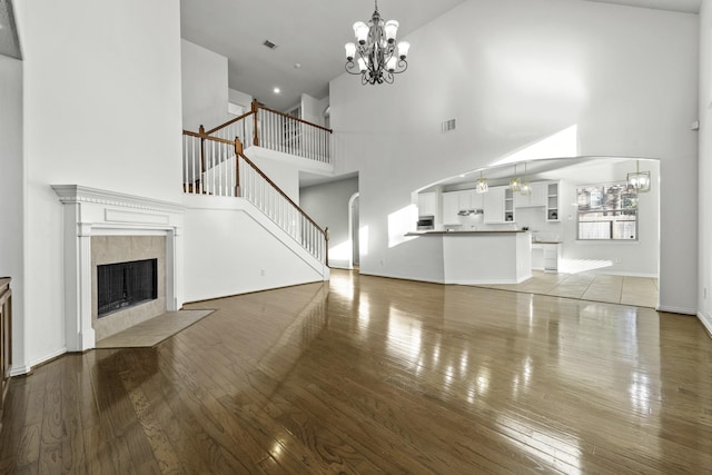 unfurnished living room with hardwood / wood-style floors, a notable chandelier, a towering ceiling, and a fireplace