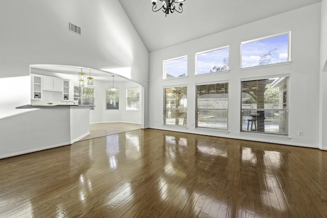 unfurnished living room with a notable chandelier, high vaulted ceiling, and dark hardwood / wood-style flooring