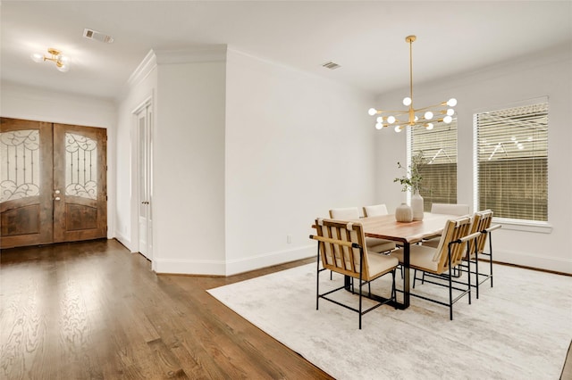 dining room with wood-type flooring, crown molding, french doors, and an inviting chandelier