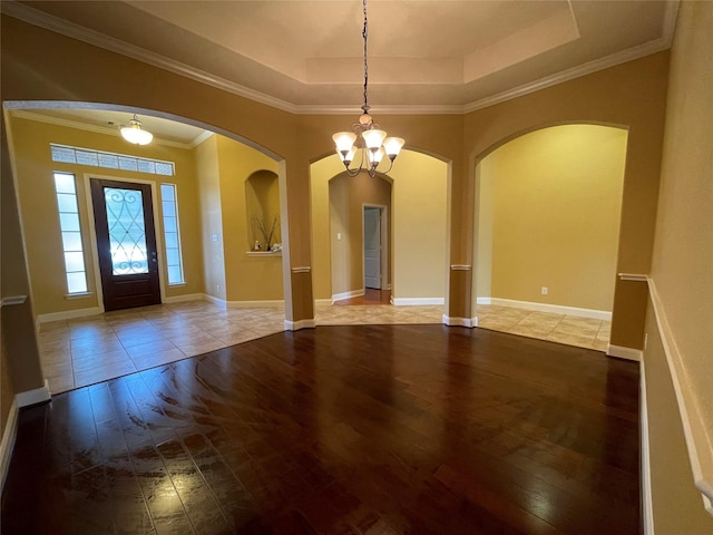 foyer with wood-type flooring, crown molding, a notable chandelier, and a raised ceiling