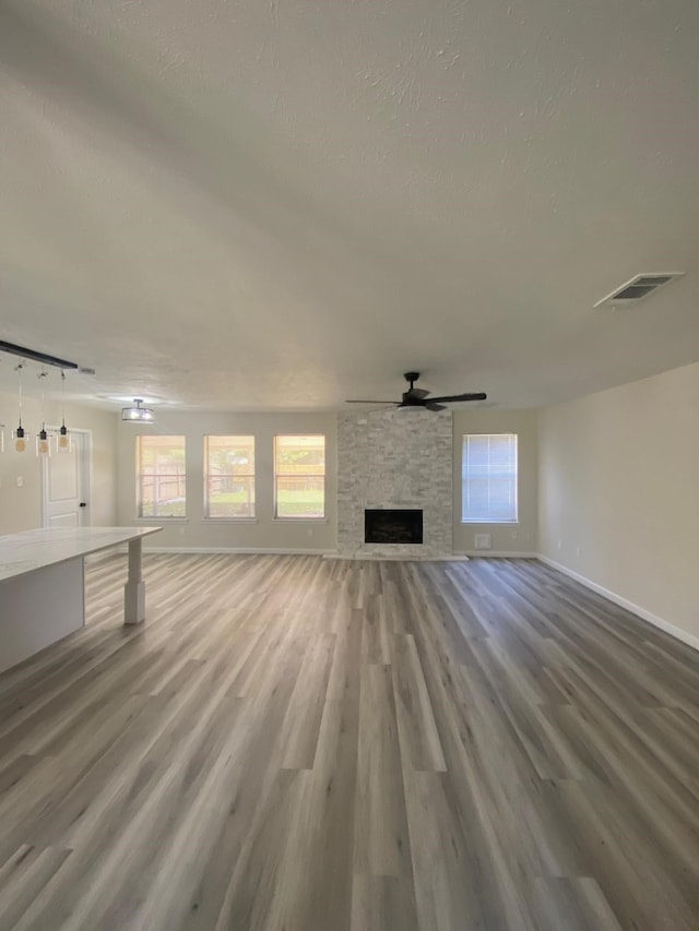 unfurnished living room featuring hardwood / wood-style flooring, ceiling fan, plenty of natural light, and a fireplace