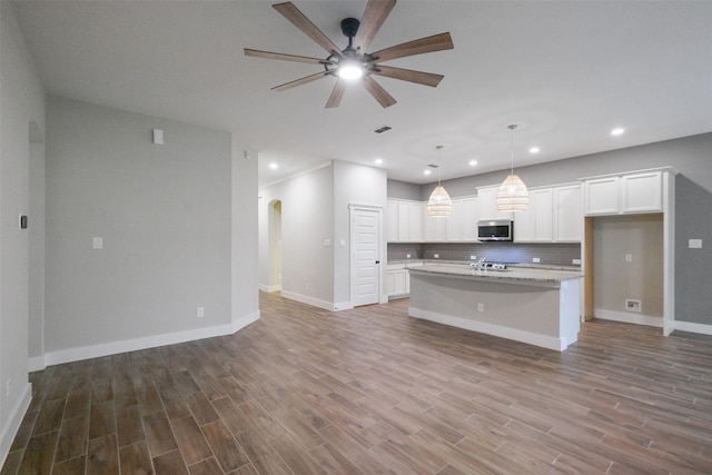 kitchen with light stone countertops, white cabinets, backsplash, hanging light fixtures, and a center island with sink